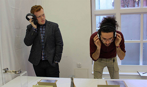 Two male students listening to an audio piece in the Healing histories exhibition with headphones
